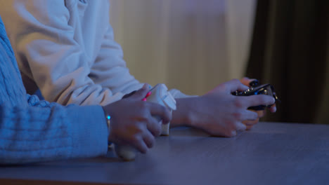 Close-Up-On-Hands-Of-Two-Young-Boys-At-Home-Playing-With-Computer-Games-Console-On-TV-Holding-Controllers-Late-At-Night-2
